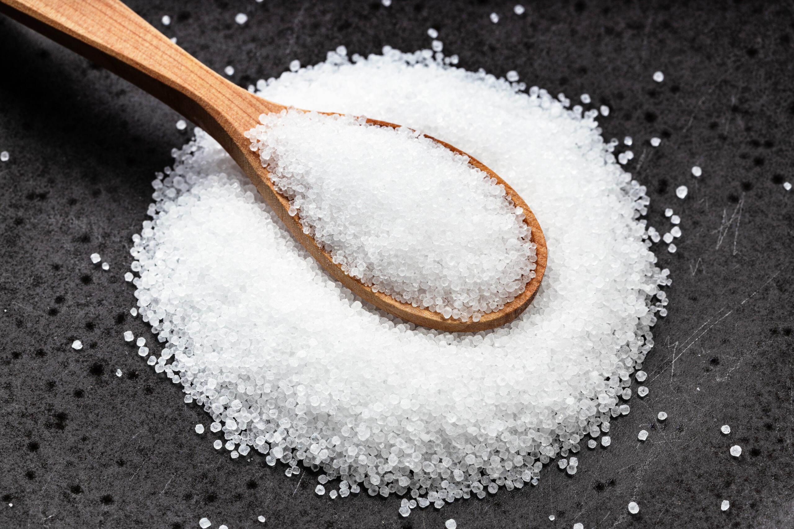 above view of wooden spoon with crystalline fructose close up on black ceramic plate